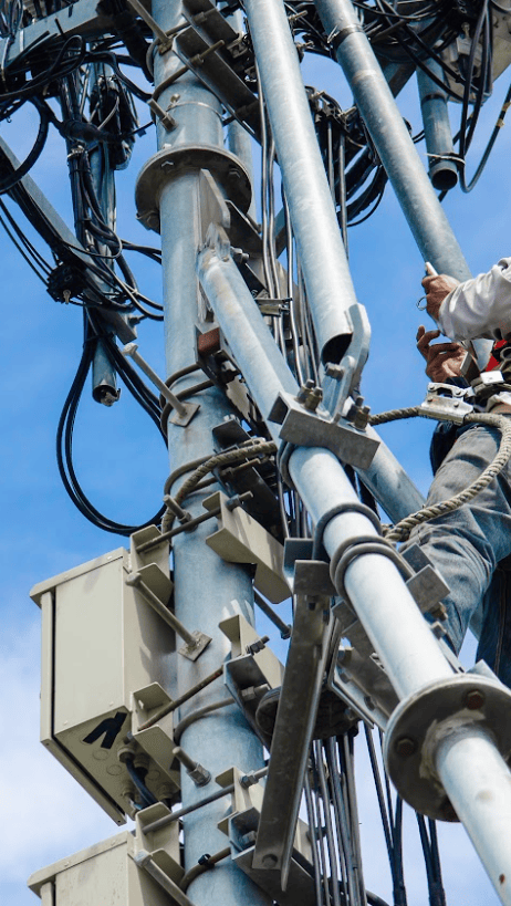 A worker wearing safety gear climbs a telecommunications tower in the APAC region