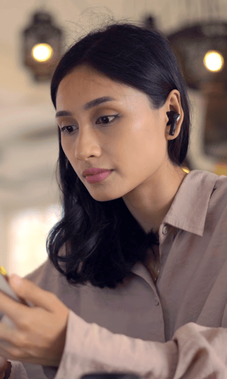A woman with long black hair looking at her phone while using wireless earbuds, capturing the modern connectivity of APAC's Talent Hub